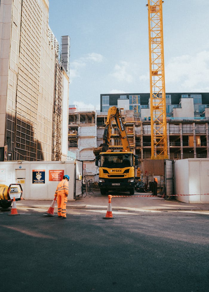City construction site featuring worker, machinery, and urban surroundings in progress under bright daylight.
